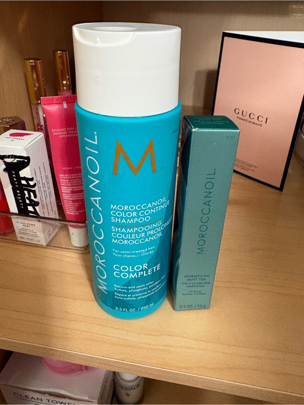 Moroccanoil Turquoise Blue Color Complete Shampoo Bottle and lip gloss in Mint.